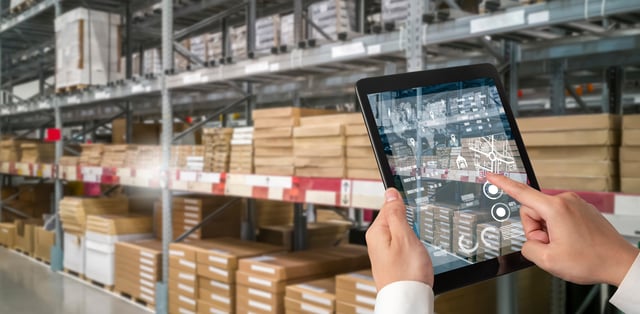 A person holding a tablet in a warehouse, displaying a 3D image of the warehouse.