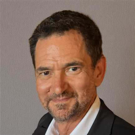 A man wearing a suit and tie, with a white shirt and a black jacket, smiling at the camera.